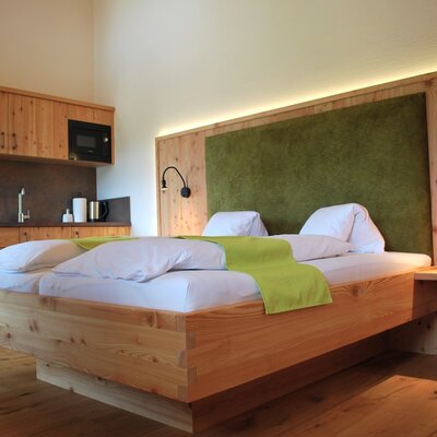 Geräumiges Schlafzimmer im Bauernhof mit Doppelbett, grüner Kopflehne und integrierter Küchenzeile mit Spüle und Mikrowelle.