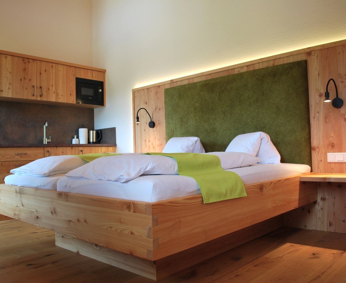 Geräumiges Schlafzimmer im Bauernhof mit Doppelbett, grüner Kopflehne und integrierter Küchenzeile mit Spüle und Mikrowelle.