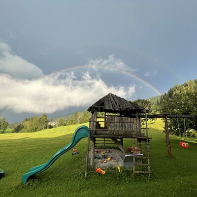 Kinderspielplatz mit Holzspielhaus, Rutsche, Sandkasten und Schaukeln.