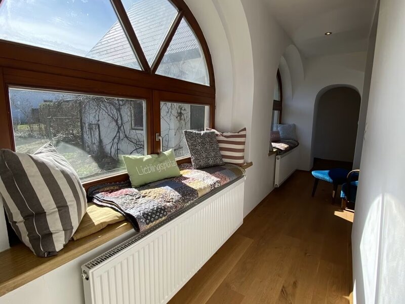 Fensterfront mit Sitzmöglichkeit, dekoriert mit bunten Decken und Pölstern