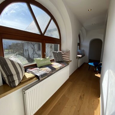 Fensterfront mit Sitzmöglichkeit, dekoriert mit bunten Decken und Pölstern Fensterfront mit Sitzmöglichkeit, dekoriert mit bunten Decken und Pölstern