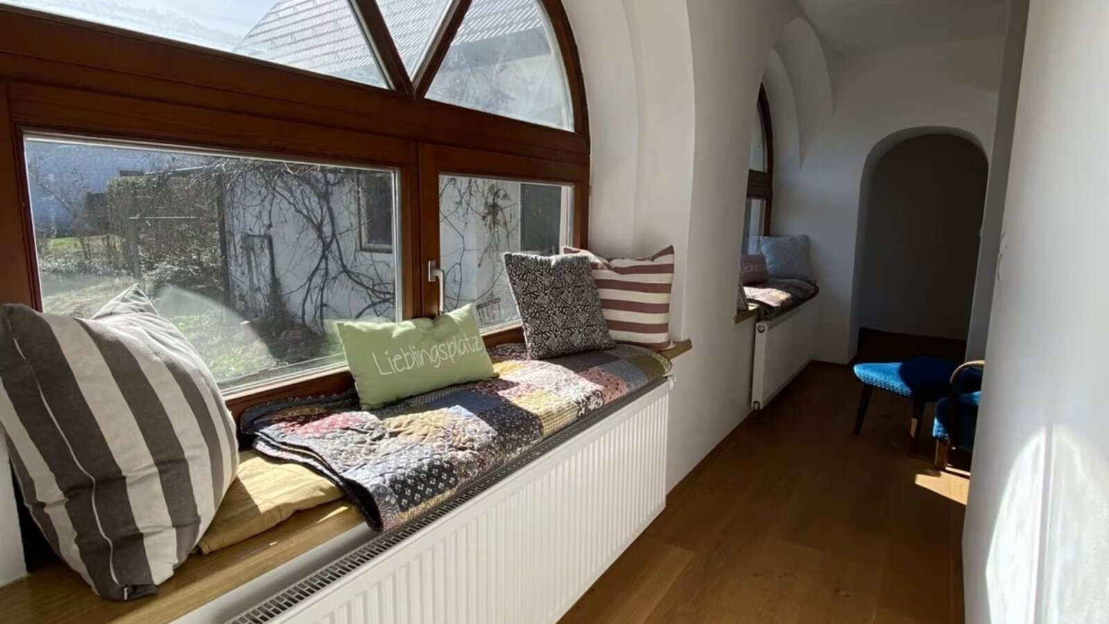 Fensterfront mit Sitzmöglichkeit, dekoriert mit bunten Decken und Pölstern