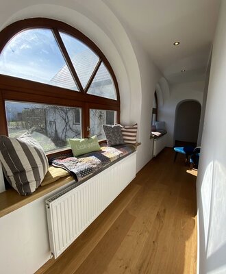 Fensterfront mit Sitzmöglichkeit, dekoriert mit bunten Decken und Pölstern