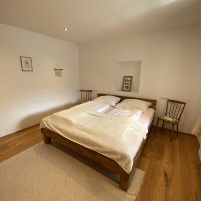 Schlafzimmer mit Doppelbett, 2 Stühle als Nachtkästchen und einer Nische, in der ein Bild steht