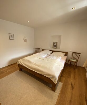 Schlafzimmer mit Doppelbett, 2 Stühle als Nachtkästchen und einer Nische, in der ein Bild steht