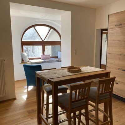 Essbereich im Bauernhof mit Holztisch, vier Barhockern und einer Fensterbank mit Sitzgelegenheit.
