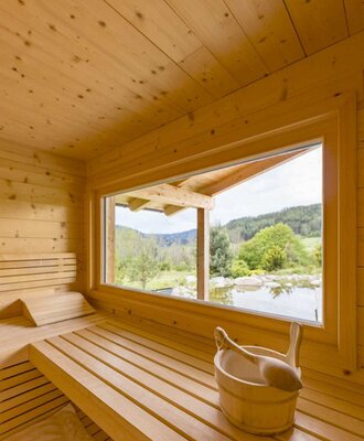 Sauna am Bauernhof mit Holzbänken und einem großen Fenster mit Blick auf die Landschaft und einen Teich. copyright: ELISABETH FRÖHLICH photography