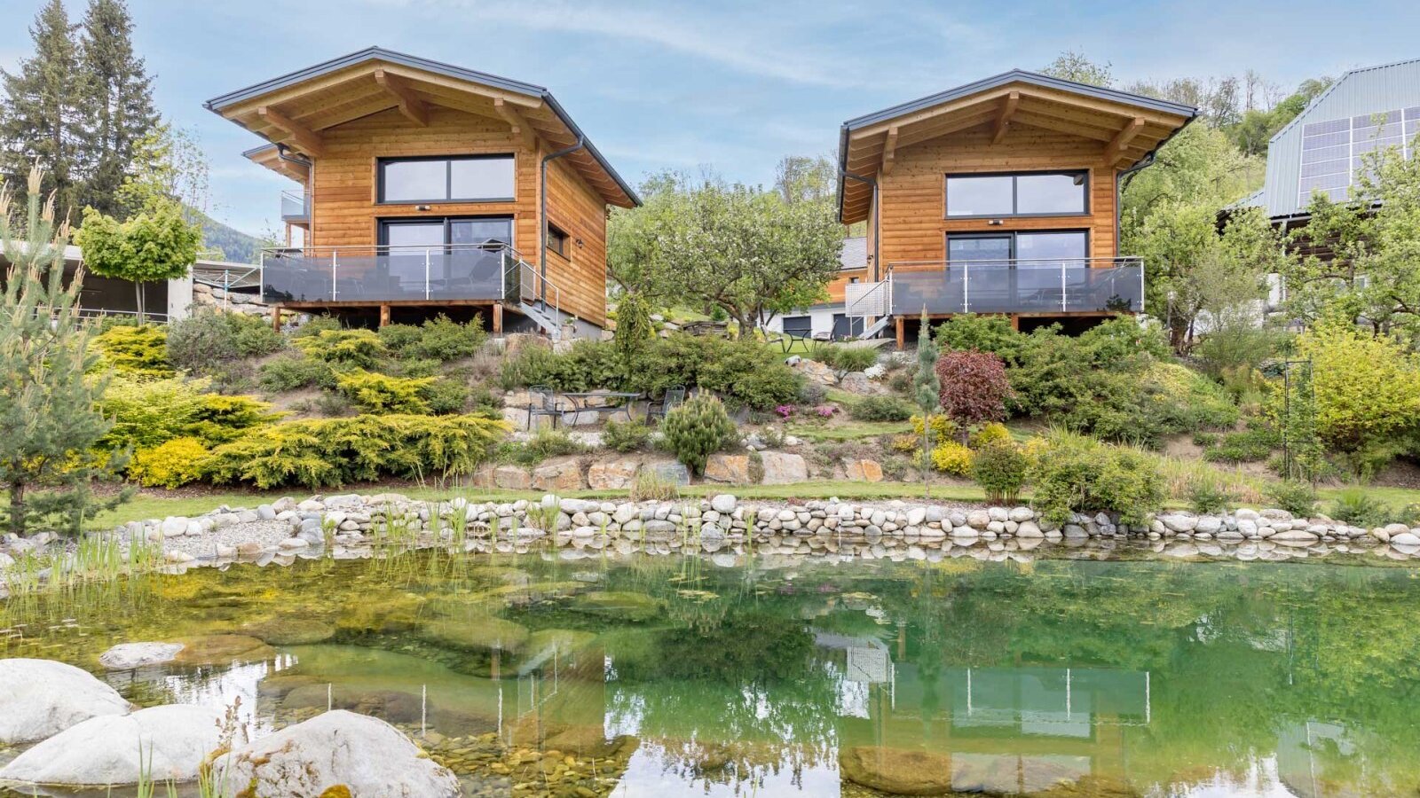 Hofchalets des Bauernhofs mit Terrassen und einem Teich im Vordergrund.