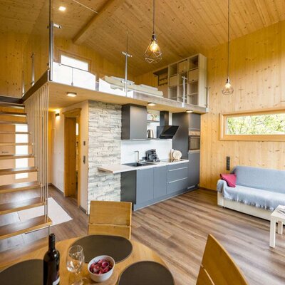 Offener Wohnbereich im Chalet mit moderner Küche, Esstisch, Sofa und Galerie mit Schlafbereich.