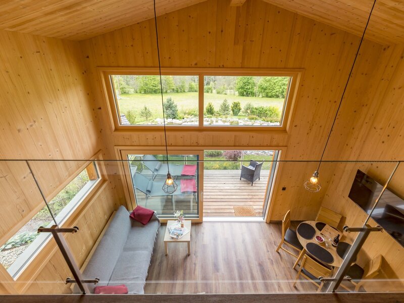Wohnbereich des Chalets mit Sofa, Esstisch, Fernseher und Zugang zur Sonnenterrasse mit Gartenblick.