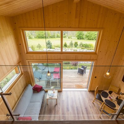 Wohnbereich des Chalets mit Sofa, Esstisch, Fernseher und Zugang zur Sonnenterrasse mit Gartenblick.