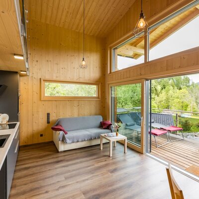 Offener Wohnbereich des Chalets mit integrierter Küche, Sofa und Zugang zur Sonnenterrasse mit Liegestühlen und Bergblick.
