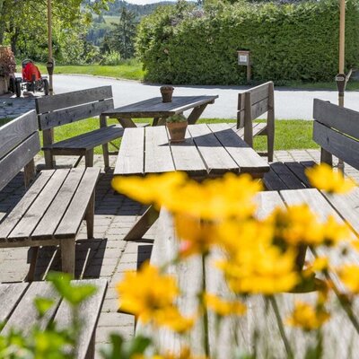 Die einladende Terrasse des Bauernhofs mit rustikalen Holzbänken und schattenspendenden Sonnenschirmen.