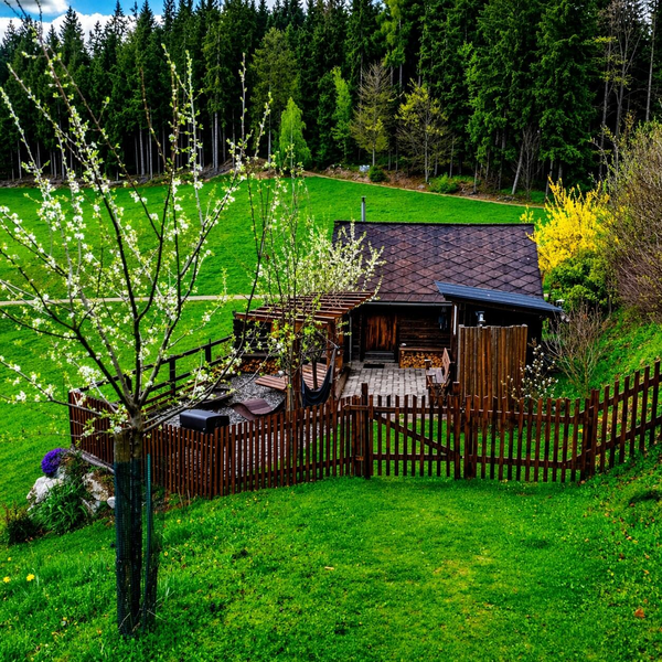 Hütte mit umzäuntem Terrassenbereich, umgeben von grünen Wiesen und Wald.