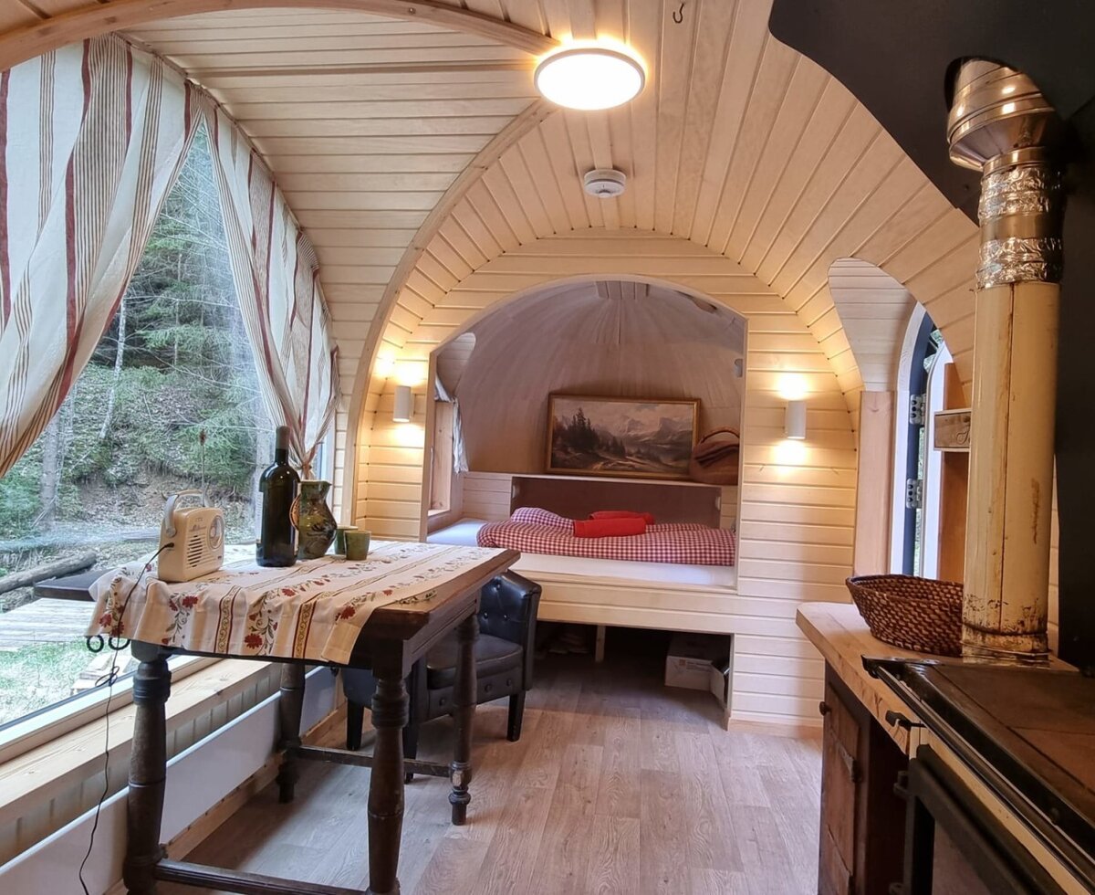 Innenansicht des Igluhaus mit Bett, Esstisch, Holzofen und Blick auf den Wald.