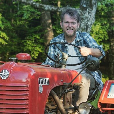 Der Gastgeber des Künstlerzimmers, Rupert Rauch,  sitzt lächelnd auf seinem roten Steyr Diesel Traktor.