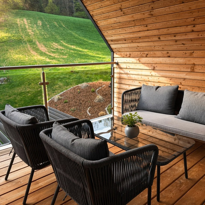 Ein einladender, holzgetäfelter Balkon mit gemütlichen Sitzmöbeln und Blick auf grüne Wiesen.