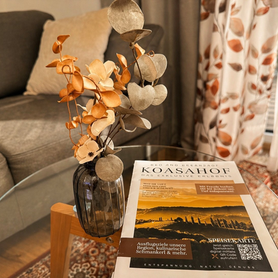 Ein eleganter Glastisch im Doppelzimmer mit stilvoller Blumendekoration und Informationsbroschüren vor einem gemütlichen Sofa.