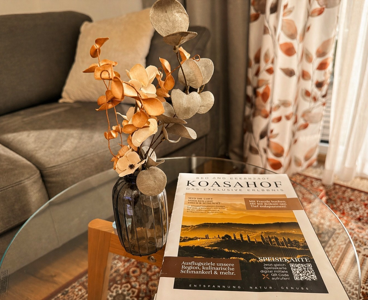 Ein eleganter Glastisch im Doppelzimmer mit stilvoller Blumendekoration und Informationsbroschüren vor einem gemütlichen Sofa.