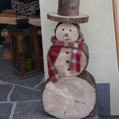 Ein dekorativer Holzschneemann mit Schal auf den Stufen des Bauernhofs.