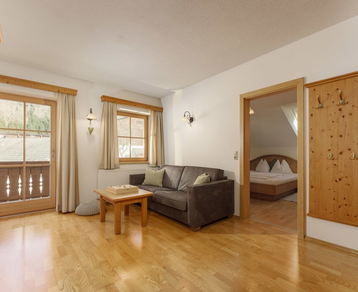 Wohnbereich des Bauernhofs mit Sofa, Couchtisch, Holzboden, handgefertigtem Holzschrank und Zugang zum Balkon, mit Blick auf das Schlafzimmer.