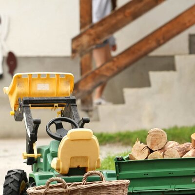 Spielzeugtraktor mit Anhänger und Holzstämmen für Kinder auf dem Bauernhof.