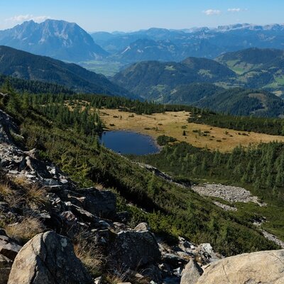 Malerischer Ausblick vom Berghang auf einen idyllischen Bergsee und die weite alpine Landschaft rund um den Bauernhof.