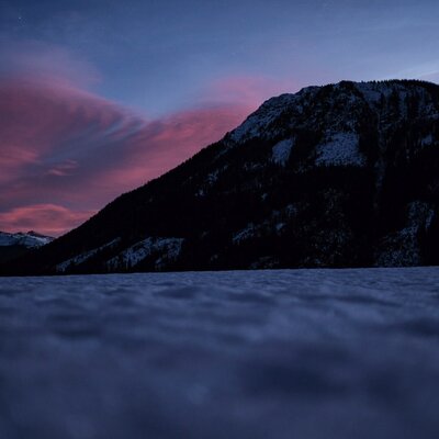 Der malerische Blick vom Bauernhof auf die verschneite Bergkulisse während einer farbenprächtigen Abenddämmerung.
