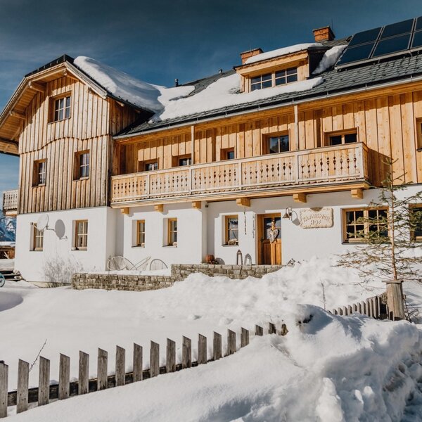 Der Bauernhof mit seiner Holzfassade, Balkonen und Solaranlagen auf dem Dach, umgeben von Schnee.