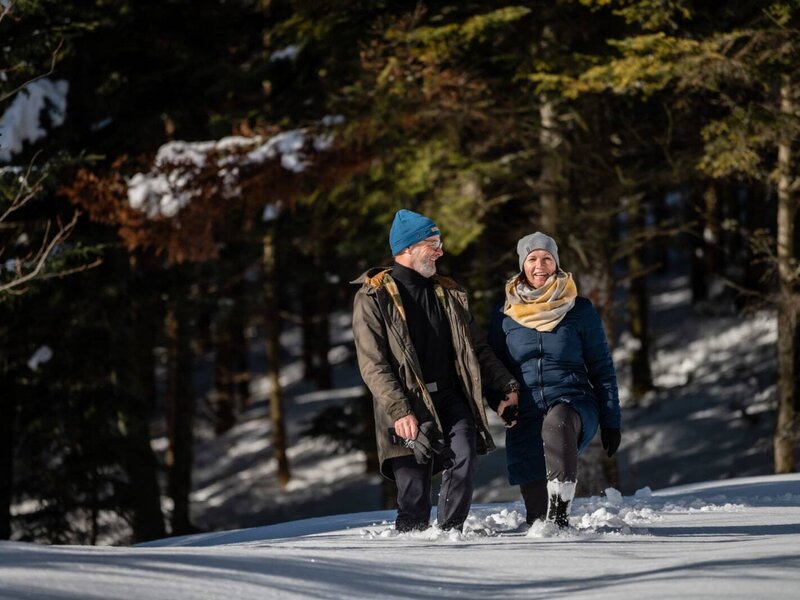 Gäste beim Winterwandern im Schnee durch den Wald in der Umgebung des Bauernhofs.