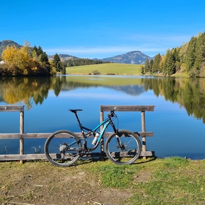 Mountainbike am Ufer des Murenteiches mit Blick auf die umliegenden Berge und Wälder, passend für aktive Gäste des Bauernhofs.