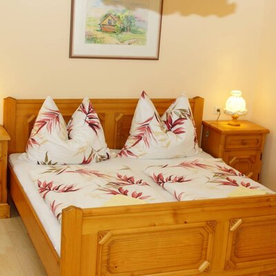 Doppelzimmer im Bauernhof mit Holzdoppelbett, zwei Nachttischen, Lampen und einem Wandbild.