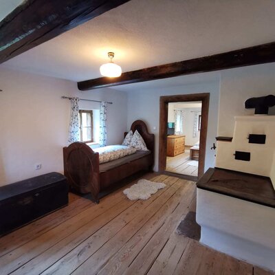 Durchgangszimmer mit zwei Einzelbetten, Holzboden, sichtbaren Deckenbalken und Tischherd