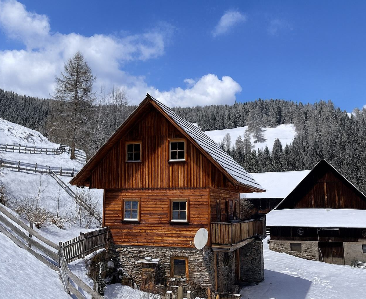 Das Bed and Breakfast Gebäude mit Holzfassade, Steinfundament und Balkon in einer verschneiten Berglandschaft.