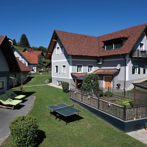 Die Außenansicht des Bauernhofs mit gepflegtem Rasen, Sonnenliegen, einer Tischtennisplatte und einem Hochbeet.