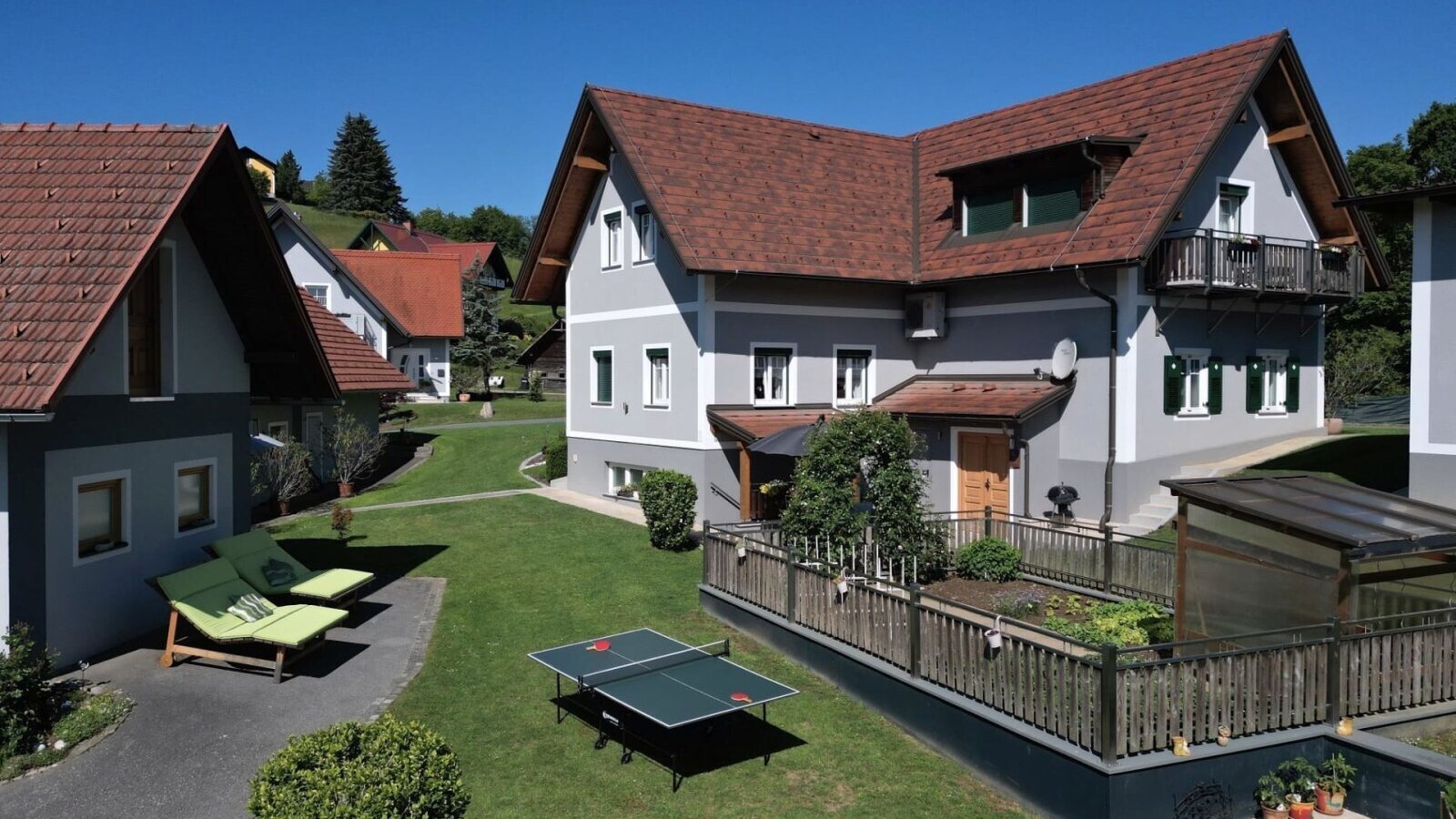 Die Außenansicht des Bauernhofs mit gepflegtem Rasen, Sonnenliegen, einer Tischtennisplatte und einem Hochbeet.