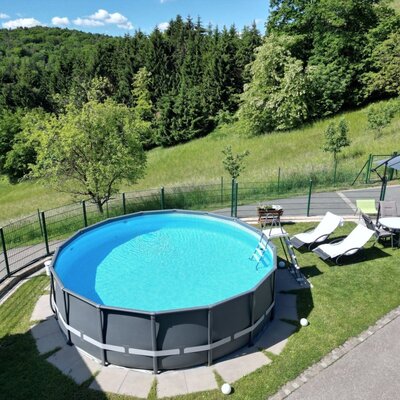 Ein runder Aufstellpool mit Liegestühlen und einem Essbereich im Freien auf dem Gelände des Bauernhofs, umgeben von Wald und Wiesen.