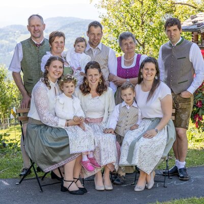 Die herzliche Gastgeberfamilie des Bauernhofs empfängt Sie in traditioneller Tracht im idyllischen Garten.