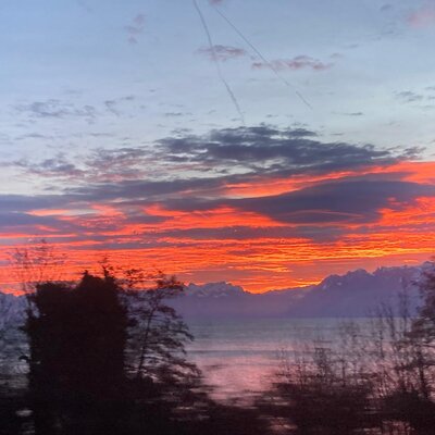 Der rote Abendhimmel über dem See und den schneebedeckten Bergen, sichtbar vom Bauernhof.