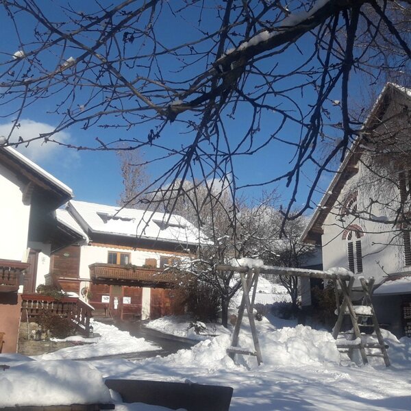 Blick auf den schneebedeckten Bauernhof mit mehreren Gebäuden, Balkonen und einem Schaukelgerüst.