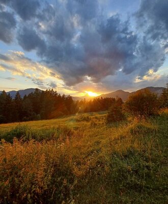 Die Wiese des Bauernhofs mit Blick auf den Sonnenuntergang über den Bergen und Wäldern.