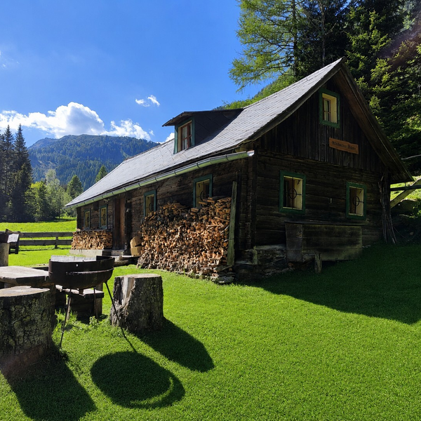 Die rustikale Holzhütte  auf einer sonnigen Wiese mit gemütlichen Sitzgelegenheiten im Freien und Bergblick.
