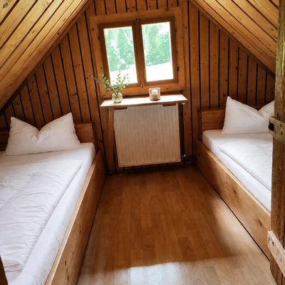 Ein gemütliches Zimmer der Hütte mit holzgetäfelten Dachschrägen, zwei Einzelbetten und einem kleinen Fenster.