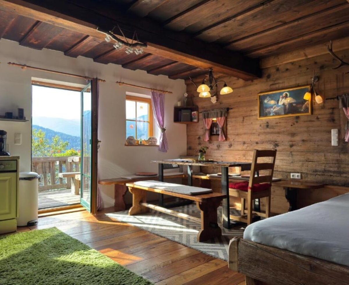 Der gemütliche Wohn- und Essbereich der Ottls Hütte mit urigen Holzwänden, einer rustikalen Sitzecke und direktem Zugang zum sonnigen Balkon.