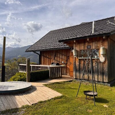 Die urige Hütte aus Holz mit einer einladenden Terrasse, einem Hot Tub und einer Grillstelle vor einer malerischen Bergkulisse.