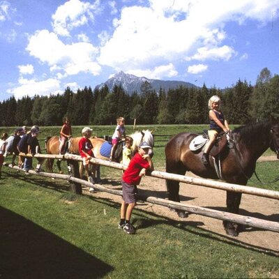 Reitmöglichkeiten für Kinder auf dem Bauernhof, mit einer Gebirgslandschaft im Hintergrund.