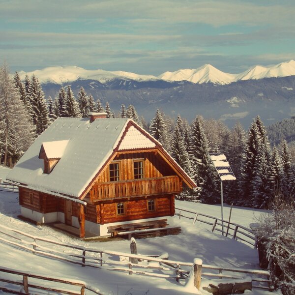 Der Hof aus Holz, umgeben von schneebedeckten Wäldern und Bergen.