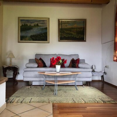 Wohnbereich des Bed and Breakfast mit Sofa, Couchtisch, Kachelofen und Wandbildern.