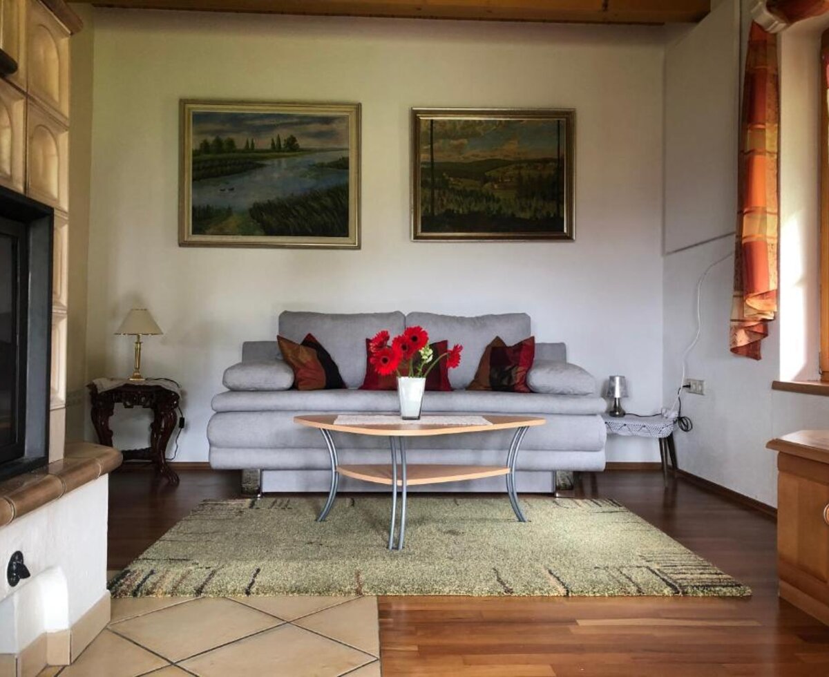 Wohnbereich des Bed and Breakfast mit Sofa, Couchtisch, Kachelofen und Wandbildern.