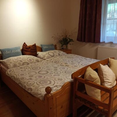 Schlafzimmer im Bed and Breakfast mit Doppelbett, zwei Nachttischen, einer Holzbank und einem Fenster mit Vorhängen.